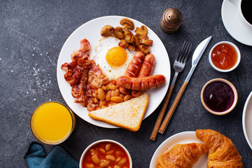 Top view flatlay with classical english breakfast with fried bacon, mushrooms and eggs. Served with orange juice, croissants and black coffee.