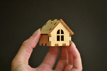 Fototapeta na wymiar Girl hand holding wooden miniature toy house on light with black background, with copyspace