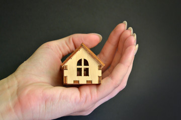 Girl hand holding in open palm wooden miniature toy house with black background, with copyspace