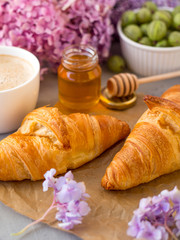 Breakfast served with coffee, croissants, natural honey jar and flowers on gray stone background. Top view.