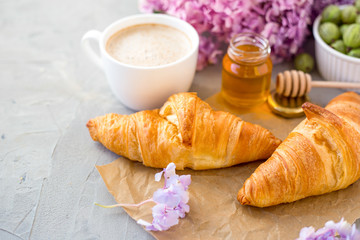 Breakfast served with coffee, croissants, natural honey jar and flowers on gray stone background. Top view.