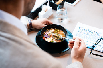 cropped view of businessman eating at table with newspaper in cafe