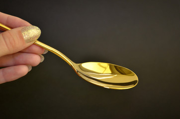 Empty golden metal spoon held by female hand with manicure on a black background, with copyspace