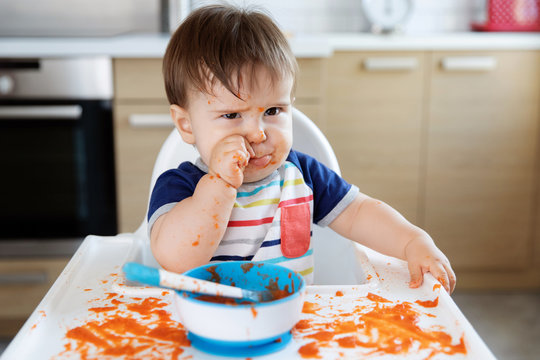 Messy baby in high chair with cute unhappy face