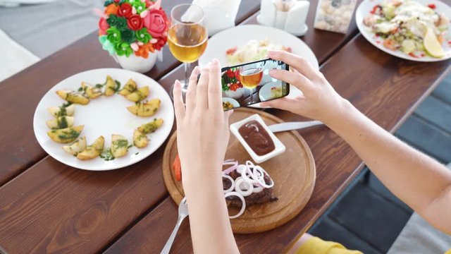Food blogger hands using smartphone taking photo of beautiful beef steak on wood table inside the cafe to share on social media. Top view food photo. Lifistyle concept.