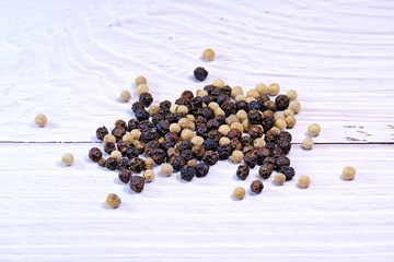Assorted spices: black and white pepper on white wooden table background.
