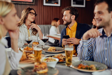 Multiethnic friends sitting at restaurant, drinking alcohol, chatting and having burgers for dinner.