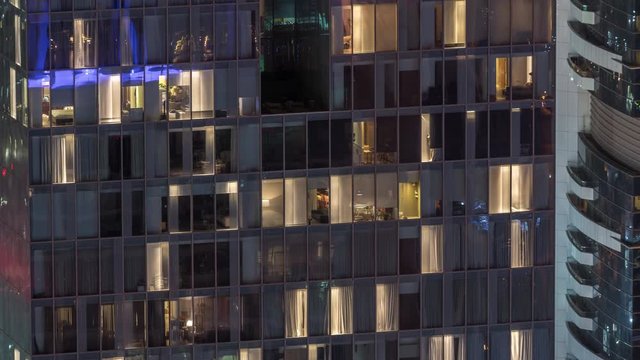 Night view of office and apartment building timelapse. High rise skyscraper with blinking windows with people moving inside. Aerial view from above. Pan up