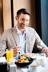 smiling businessman looking at camera while eating in cafe