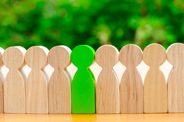 Wooden figures of people. Green man stands out from the crowd of workers. The concept of choosing a...
