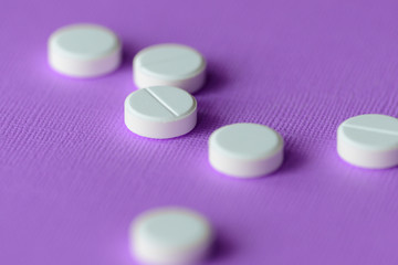 White tablets scattered on a purple background close up
