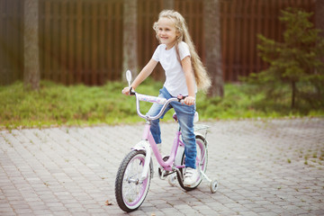 Cute little smiling girl riding bike bicycle in a courtyard on sunny summer day. Active family leisure with kids. 