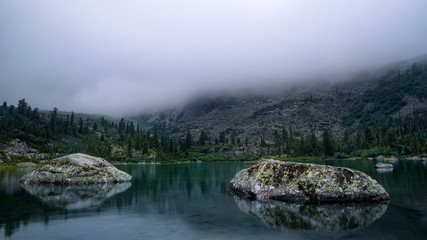 Blue lake with reflection of stones in heavy fog Ergaki