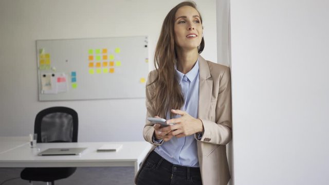Young businesswoman standing in office talking through phone on wireless earphones