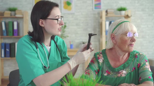 Otolaryngologist examines the ear of an old woman with the help of an otoscope
