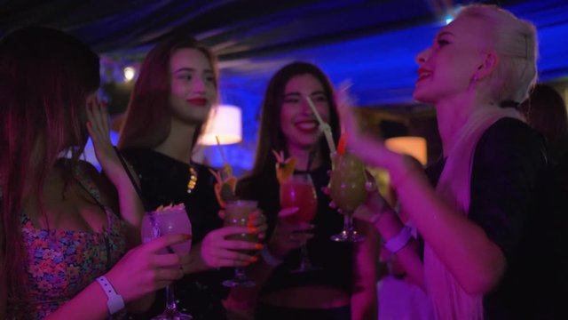 celebrate in a nightclub, young sexy females friends in fashionable clothes have fun at girls party drinking alcohol cocktails