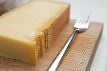  slice of Austrian mountain cheese with rind on a wooden plate with a fork