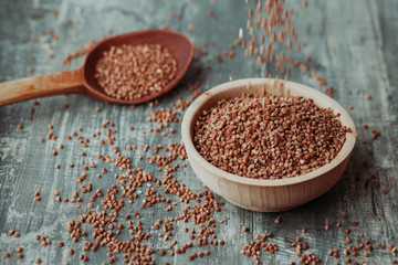 Close-up photo of dry  buckwheat in a wooden plate with a wooden spoon. Free space for text mockup