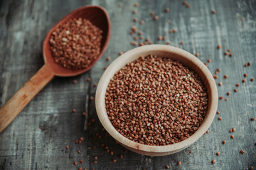 Close-up photo of dry  buckwheat in a wooden plate with a wooden spoon. Free space for text mockup