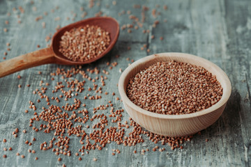 Close-up photo of dry  buckwheat in a wooden plate with a wooden spoon. Free space for text mockup