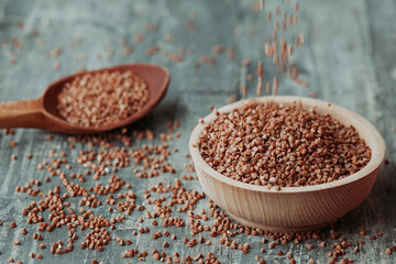 Close-up photo of dry  buckwheat in a wooden plate with a wooden spoon. Free space for text mockup