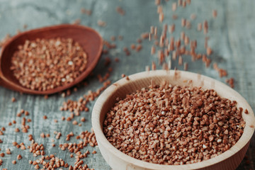 Close-up photo of dry  buckwheat in a wooden plate with a wooden spoon. Free space for text mockup