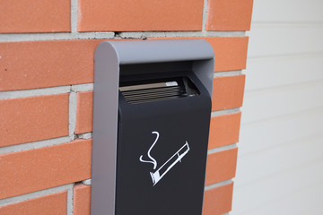 Vertical metal ashtray with a smoking cigarette image on a red brick wall, closeup - 282630688