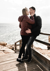 Couple in love standing on stairs near ocean. Attractive pair enjoying ocean view on wooden path....