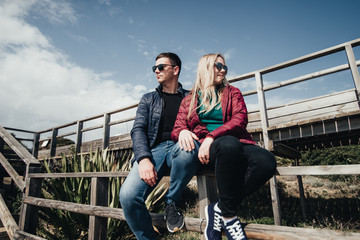 Couple in love sitting on stairs near ocean. Attractive pair enjoying ocean view on wooden path....