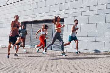 Full length of young people in sports clothing jogging while exercising on the sidewalk outdoors
