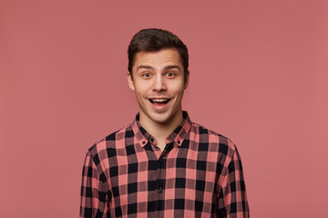 Young handsome happy amazed guy in checkered shirt, looks at the camera with surprised expression,...