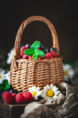 Fototapeta na wymiar Raspberries and blueberries in a basket with chamomile and leaves on a dark background. Summer and healthy food concept. Selective focus.