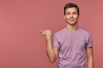 Young attractive cheerful guy wears in blank t-shirt, looks at the camera and smiles, wants to turn...