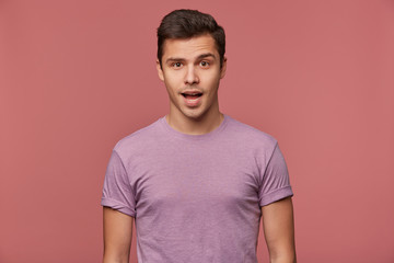 Obraz premium Photo of handsome cheerful guy wears in blank t-shirt, looks at the camera with happy expression, stands over pink background.