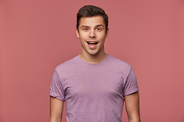 Portrait of handsome cheerful guy wears in blank t-shirt, looks at the camera with happy amazed expression, stands over pink background.