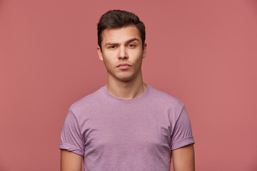 Portrait of handsome doubting young man wears in blank t-shirt, looks at the camera with raised...