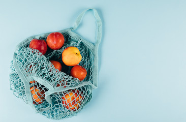 Mesh shopping bag with fruits plims and peach on blue background. Top view, flat lay, copy space. Zero waste, eco friendly concept.
