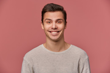 Portrait of handsome young cheerful man wears in blank long sleeve, looks at the camera with happy expressions, stands over pink background.