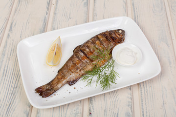 appetizing fried fish, beautifully laid out with greens and vegetables on a dish, for designer solutions in cooking	
