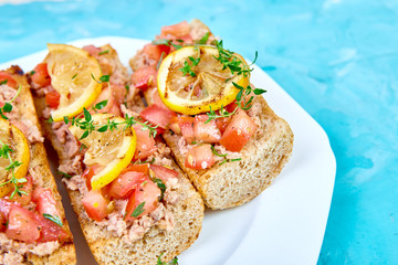 Appetizer bruschetta with tuna and tomatoes in white plate on blue background. Italian cuisine. Delicious Italian antipasti crostini. Copy space.