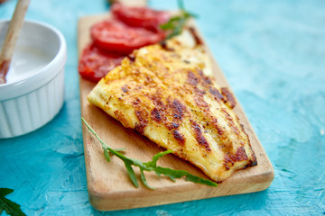 Grilled pike fillet with tomatoes on wooden board on blue background. Grilled seafood. Barbecue fish. Copy space. Healthy food.
