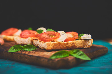 Caprese bruschetta toasts on cutting board. Bruschetta with tomatoes, mozzarella cheese and basil on a green background. Traditional italian appetizer or snack, antipasto
