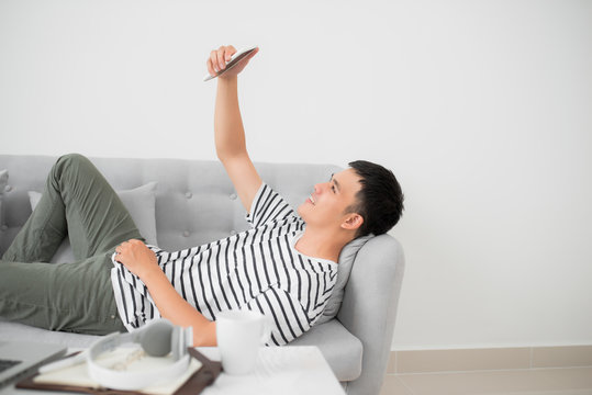 Asian Young Man Using Mobile Phone While Lying Indoor.