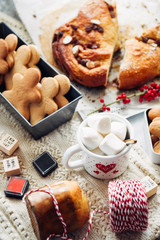 Christmas cookied and cakes with a mugs full of marshmallows, preparation of cokies and cakes for christmas, arranged on a tabletop with christmas decoration