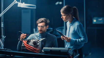 Male and Female Automotive Engineers with a Tablet Computer and Inspection Tools are Having a Conversation While Testing an Electric Engine in a High Tech Laboratory with a Concept Car Chassis.