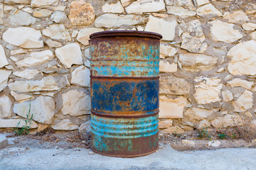 Obraz premium Big rusty blue barrel stand near a stone wall in the backyard.