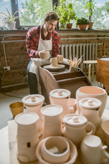 Young successful potter in workwear working over new clay item in his own workshop