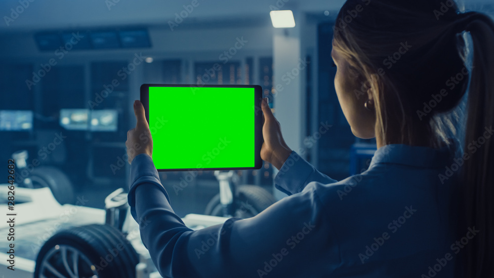 Aufkleber Female Engineer Holds a Tablet Computer with Green Screen Mock Up and Looks at Electric Car Chassis Prototype with Wheels, Batteries and Engine Standing in a High Tech Development Laboratory.