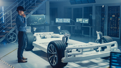 Fototapeta premium Automotive Engineer Working on Electric Car Chassis Platform, Using Augmented Reality Headset. In Innovation Laboratory Facility Concept Vehicle Frame Includes Wheels, Suspension, Engine and Battery.