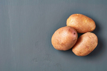 Heap of fresh raw potatoes lies on dark scratches concrete. Space for text. Top view